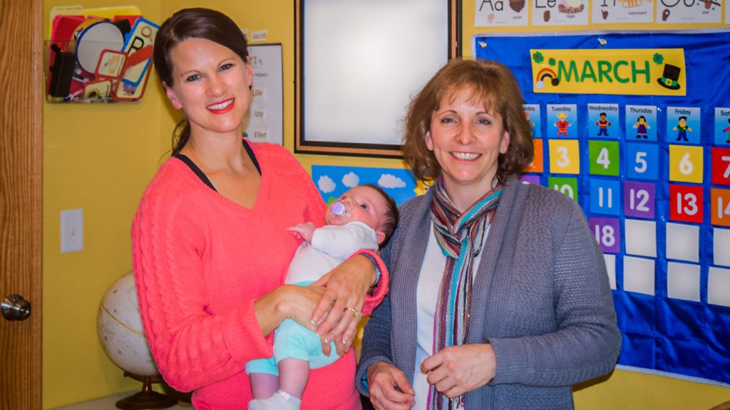 Two women holding a baby in a classroom.