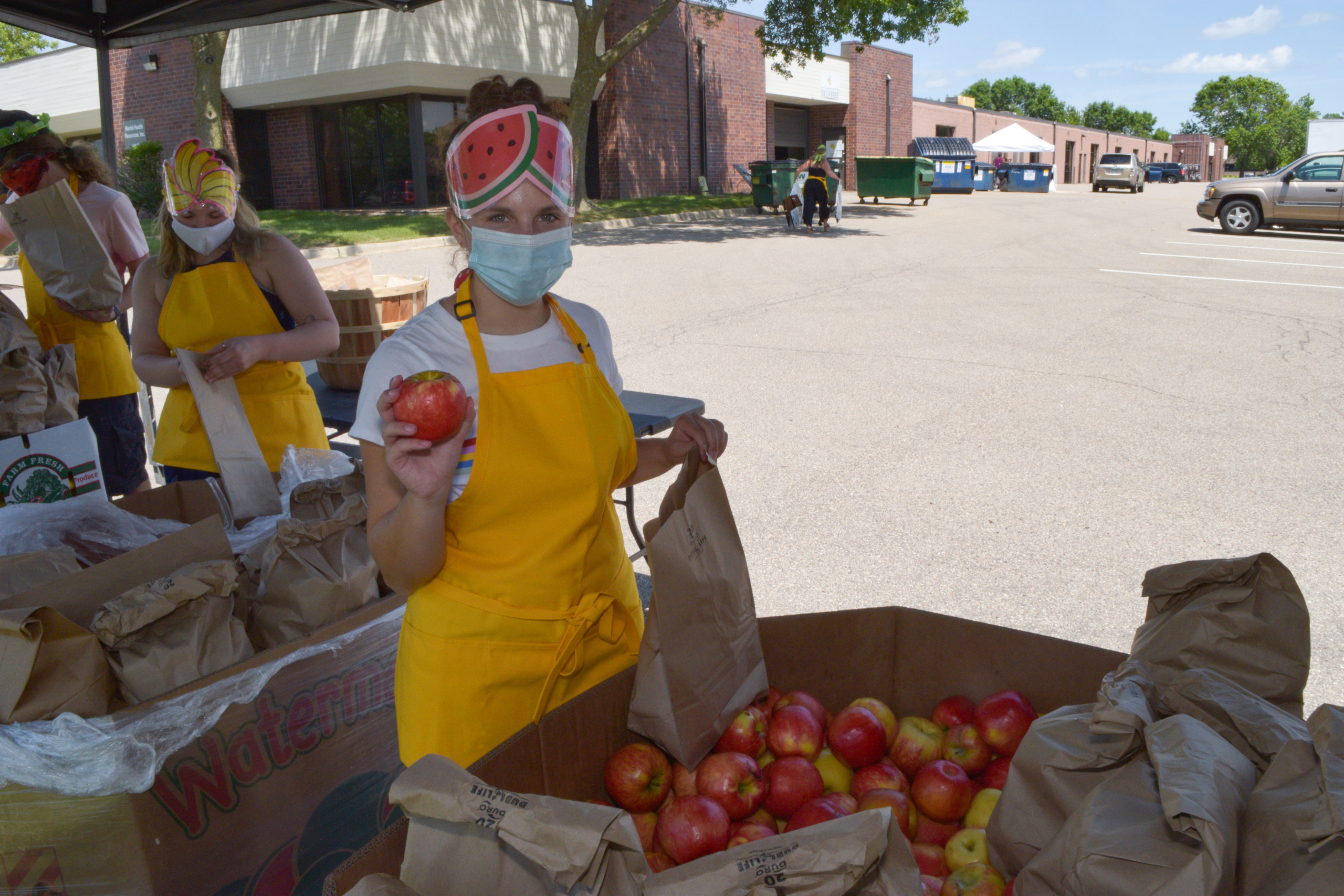 woman in a mask with an apple at the farmers markets produce stand